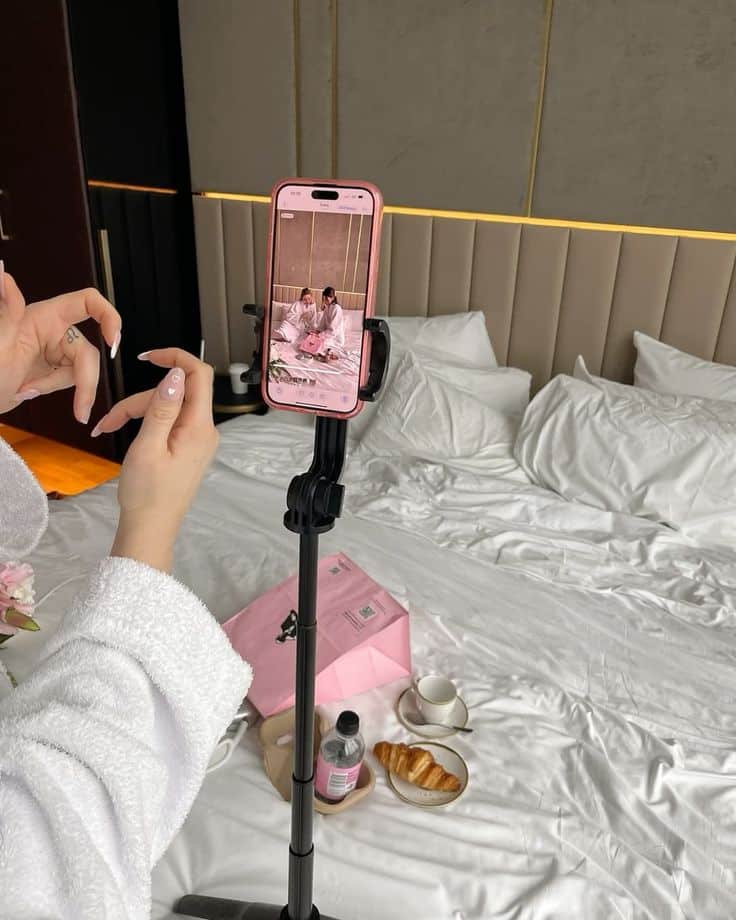Person recording on phone in cozy bedroom with breakfast, wearing bathrobe. Perfect morning vibe captured on camera.