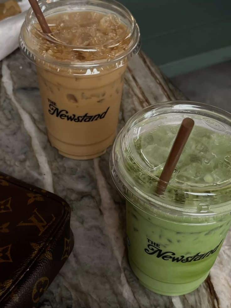 Two iced drinks, coffee and matcha, on a marble table at The Newstand cafe. Luxurious purse in view. Refreshing and stylish.