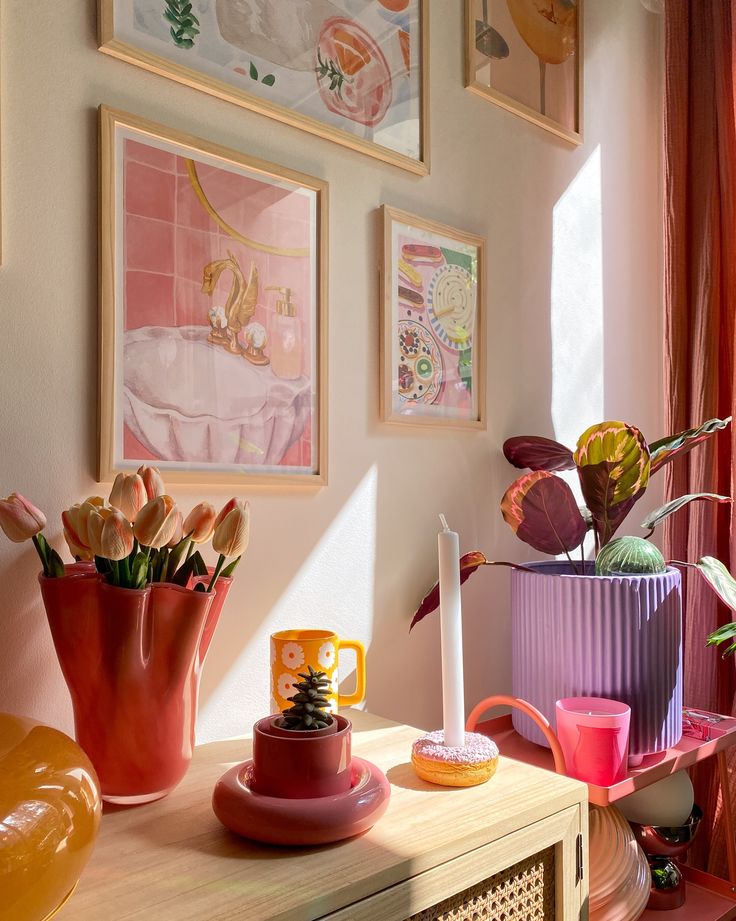 Colorful living room with framed art, tulips in a red vase, and a stylish candle display on a sunlit wooden table.