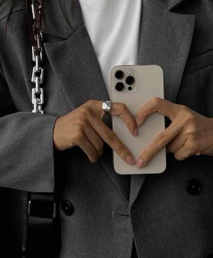 Person in a gray blazer forming a heart shape with hands over a smartphone, symbolizing love for technology.