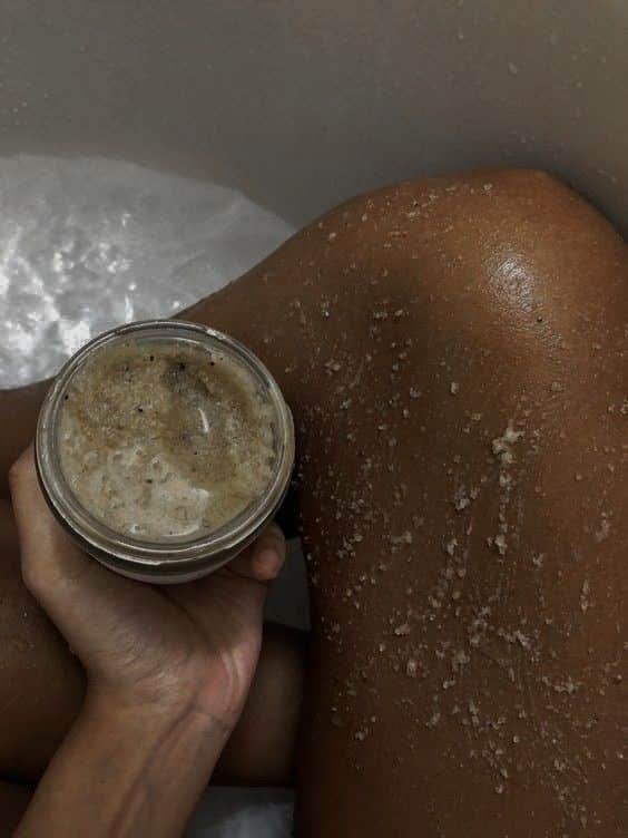 Close-up of a person applying a homemade exfoliating scrub to their leg, showcasing smooth skin care routine in a bath setting.