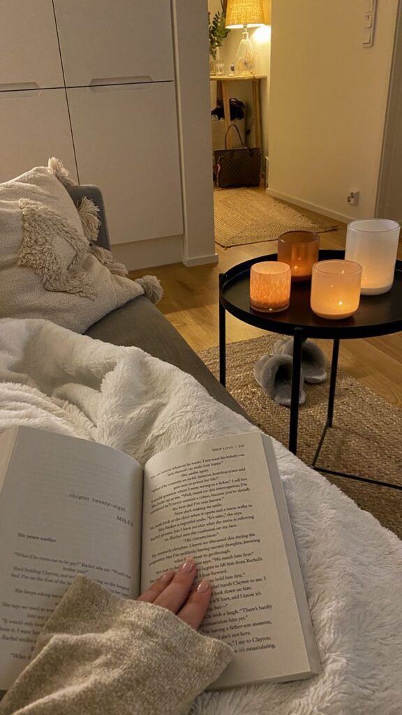 Cozy reading nook with soft blanket, candles, and an open book, creating a warm and relaxing ambiance in a stylish living room.