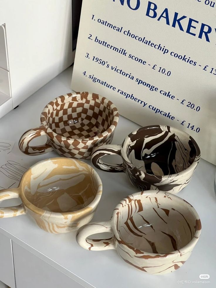 Four marbled ceramic mugs in various patterns on a white shelf with a bakery menu in the background.