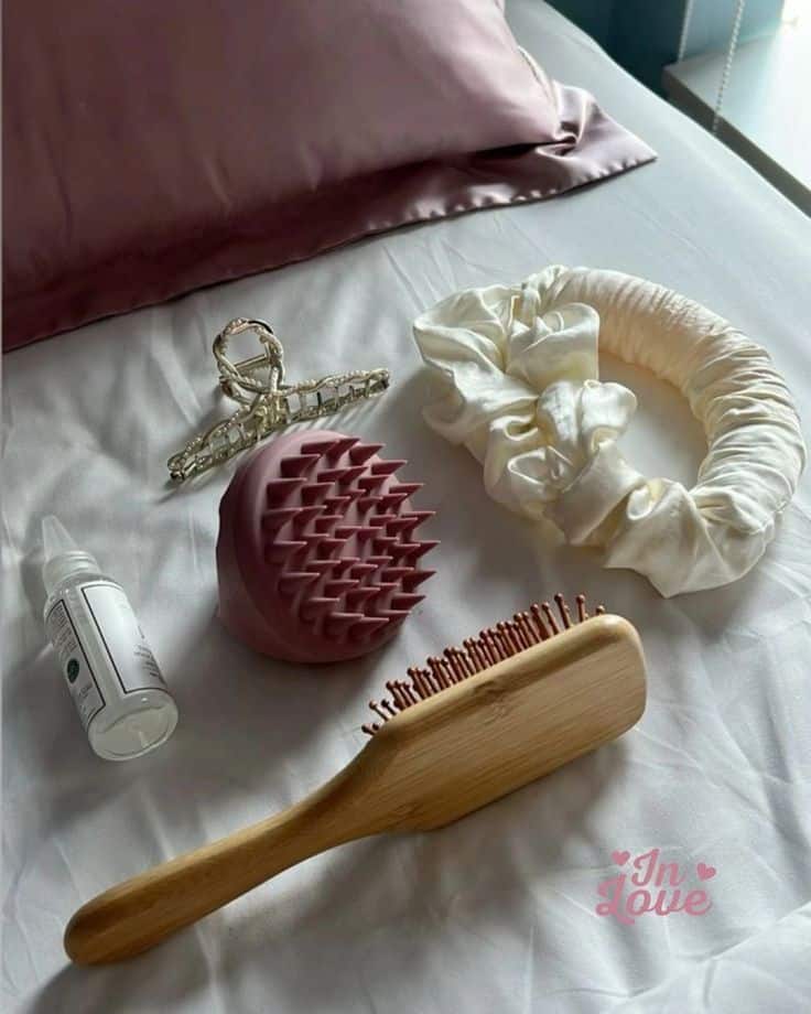 Hair care essentials on a bed: silk pillow, hairbrush, scalp massager, scrunchies, and hair oil. Perfect for a calming beauty routine.