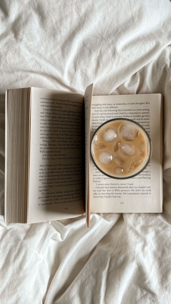 Open book with iced coffee on a cozy bed. Perfect for a relaxing reading session.