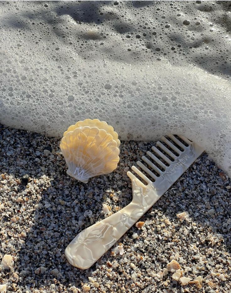 Seashell and vintage comb on sandy shore with gentle surf foam, creating a serene beach scene.