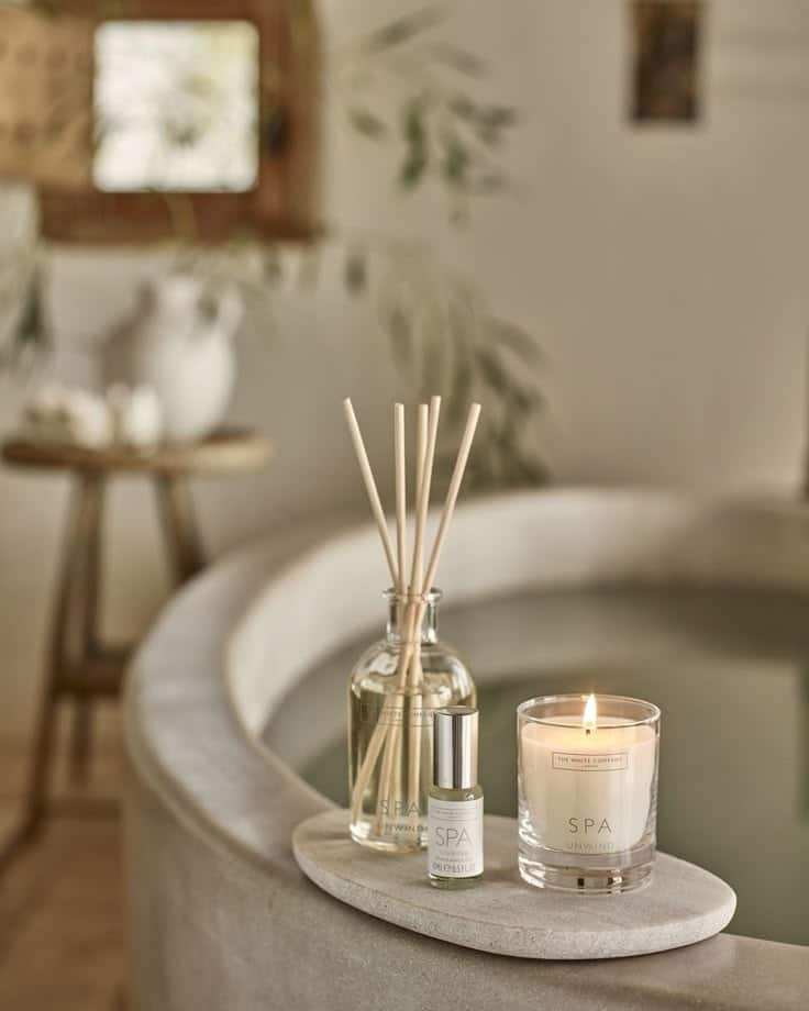Spa relaxation scene with reed diffuser, essential oil, and lit candle by a serene bathtub, creating a calming ambiance.
