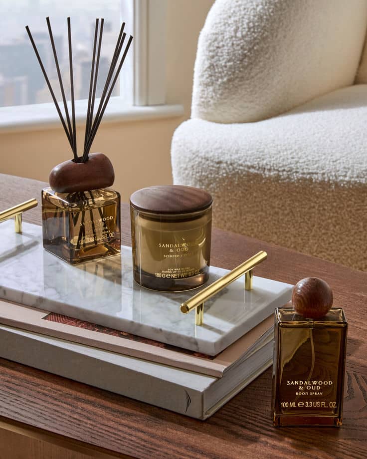 Sandalwood and oud fragrance set with diffuser, candle, and room spray on a marble tray in a cozy, modern living space.