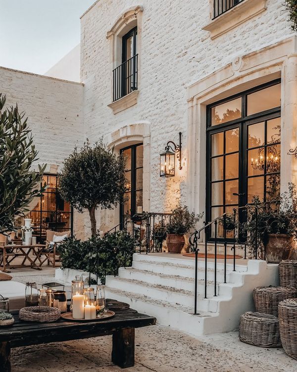 Elegant Mediterranean villa courtyard with rustic decor, surrounded by plants, candles, and cozy evening lighting.