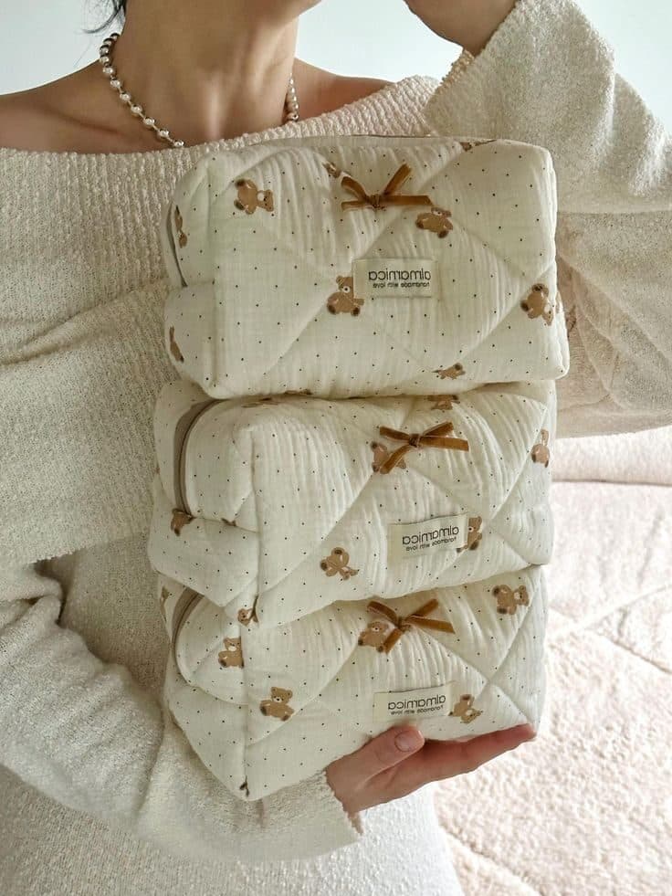 Stack of three quilted, teddy bear patterned pouches held by a person in cream sweater, showcasing cozy storage solutions.