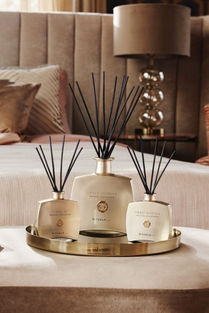 Luxury home fragrance diffusers on a tray enhance cozy bedroom decor with elegant lamp and plush pillows.