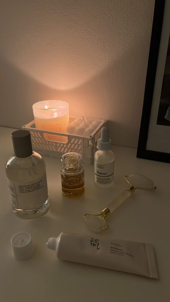 Cozy skincare setup with candle, oils, serum, and a jade roller on a calm evening. Skincare essentials for a relaxing routine.