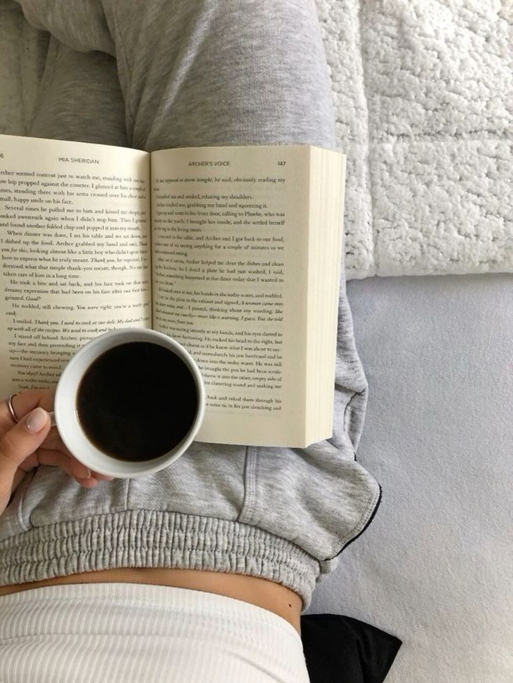 Cozy morning with a book and coffee in bed, wearing comfy gray sweatpants and a white top. Perfect relaxation setup.