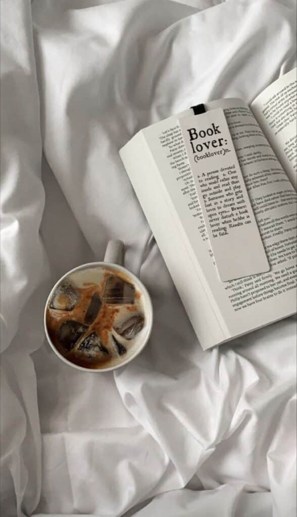 Cozy bed scene with open book and iced coffee, perfect for book lovers seeking relaxation and comfort.