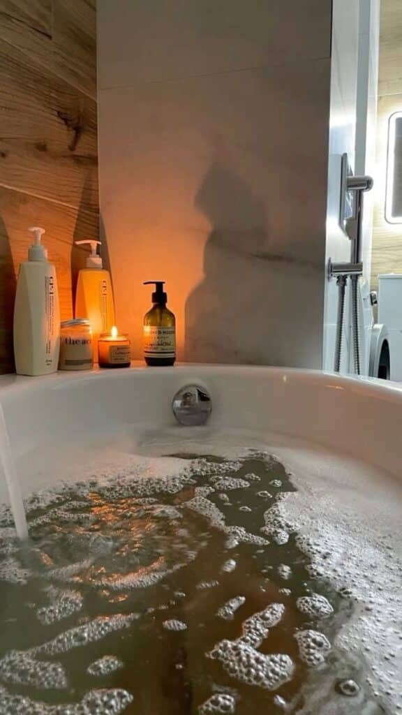 Calm bathroom scene with candles, bubbles, and bath products in a relaxing soak setup. Perfect for unwinding and self-care.
