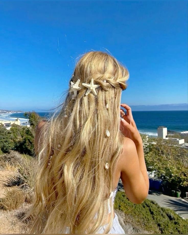 Woman with long blonde hair and beach-themed accessories, overlooking a coastal view under a clear blue sky. Perfect summer vibe.