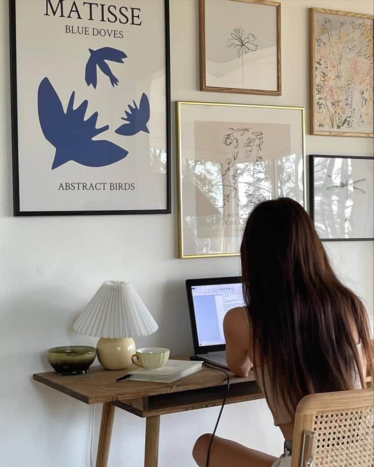 Woman working at a laptop in a cozy home office with wall art and decor.