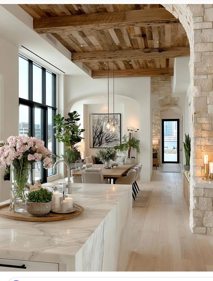 Modern kitchen and dining area with marble countertop, wooden ceiling, and elegant decor featuring flowers and plants.