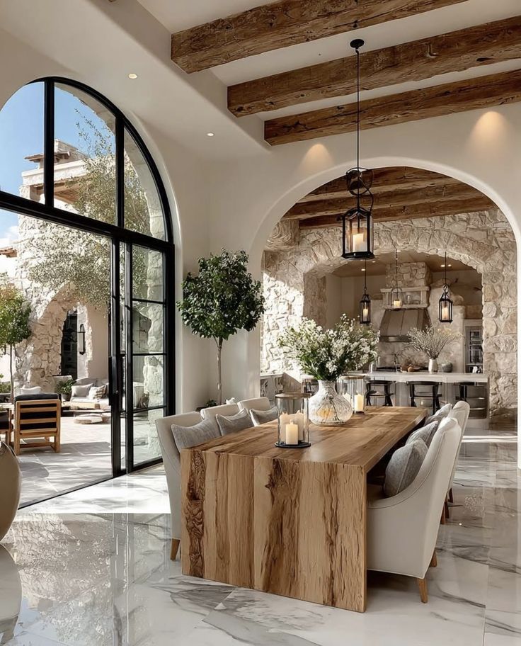 Stylish open dining area with natural wood table, plush chairs, stone archway, and modern decor under rustic beams.