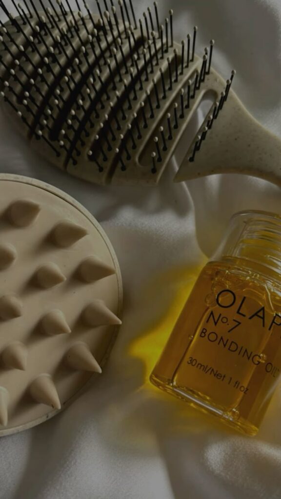 Hair tools and Olaplex No.7 Bonding Oil on white fabric, promoting haircare essentials for smooth, shiny hair.