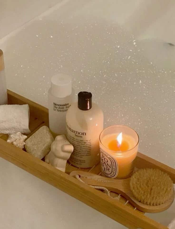 Relaxing bath setup with a candle, body wash, brush, and soap on a wooden tray against a backdrop of bubbles. Perfect for self-care.