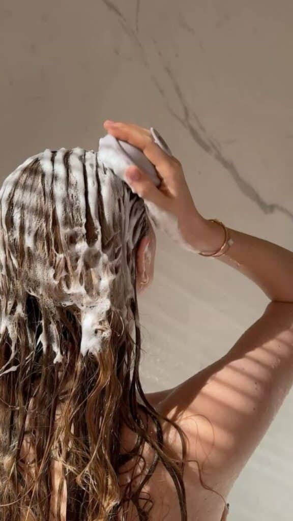 Person washing hair with shampoo, lathering up in the shower; clean hair care, hygiene routine, and self-care concept.