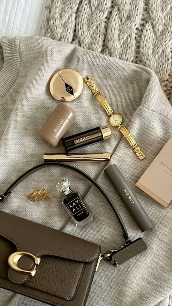 Luxury flat lay with makeup, perfume, and accessories on a cozy sweater, perfect for a chic and sophisticated look.