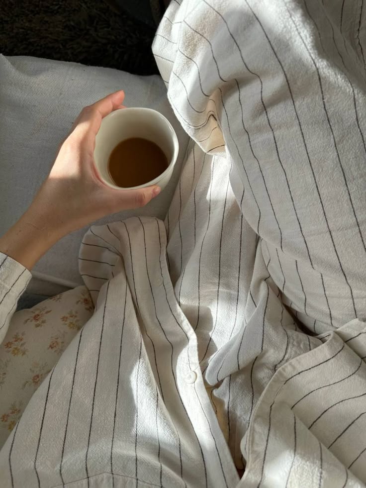 Cozy morning with a cup of coffee in hand, wearing striped pajamas in soft light. Relaxing start to the day.