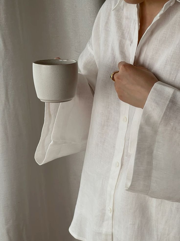 Person in white shirt holding a ceramic mug, showcasing minimalist style and comfort in a soft-lit setting.