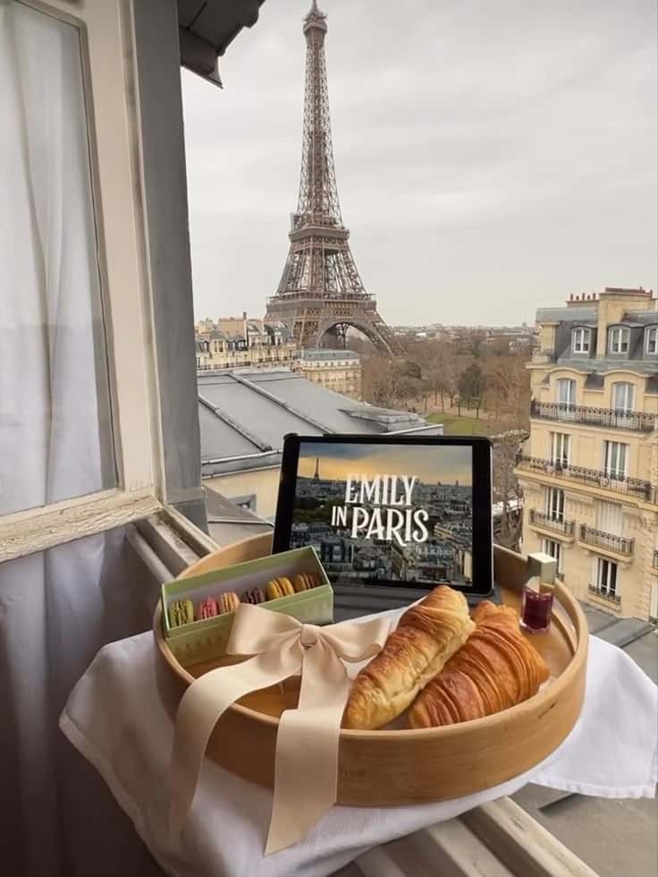 Parisian breakfast with croissants and macarons, Eiffel Tower view, and a tablet displaying a French TV show.