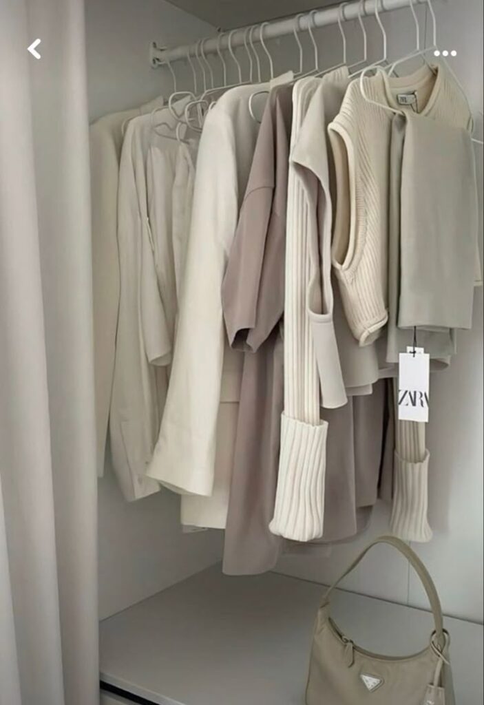 Neutral-toned clothing hanging in a closet with a beige handbag below. Perfect for minimalist style inspiration.
