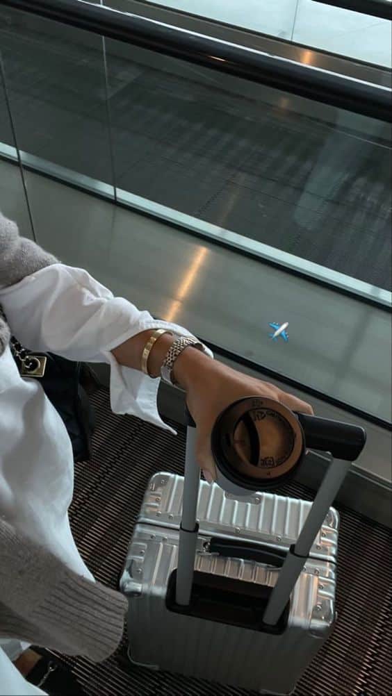 Traveler holding coffee, a stylish handbag, and silver carry-on suitcase at airport terminal. Ready for an adventure! ✈️