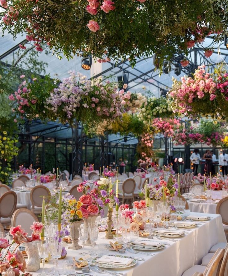Lush floral decor adorns elegant outdoor wedding reception with beautifully arranged tables and vibrant hanging flowers.