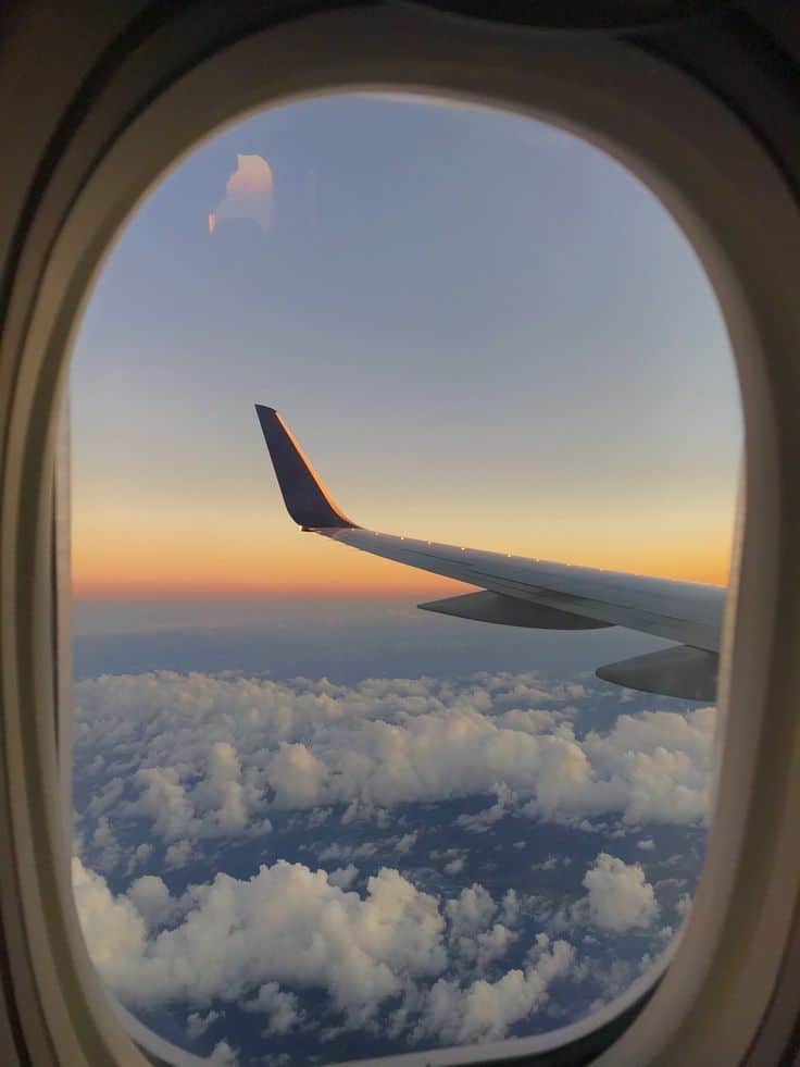 View from airplane window at sunset, showing a wing over fluffy clouds and vibrant sky. Ideal travel inspiration.