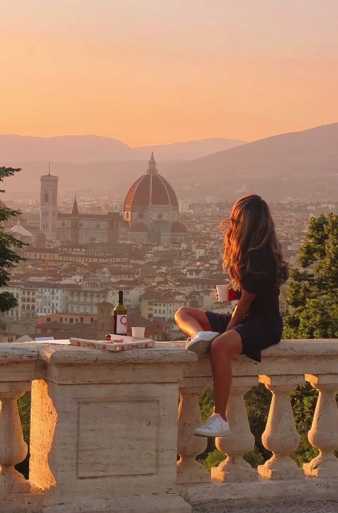 Woman enjoying sunset view of Florence skyline with wine and pizza, overlooking Florence Cathedral from a scenic terrace.