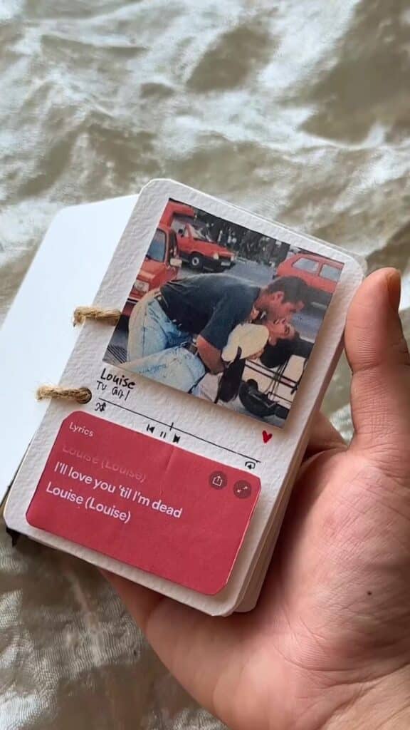 Hand holding a scrapbook with a kissing couple photo and lyrics, I'll love you 'til I'm dead from a song. Romantic memory keepsake.
