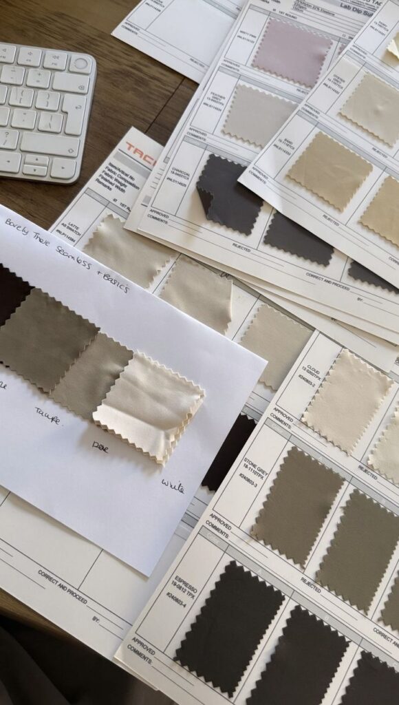 Fabric swatches and color samples on a desk, featuring neutral tones like taupe, dove, and white, alongside a keyboard.