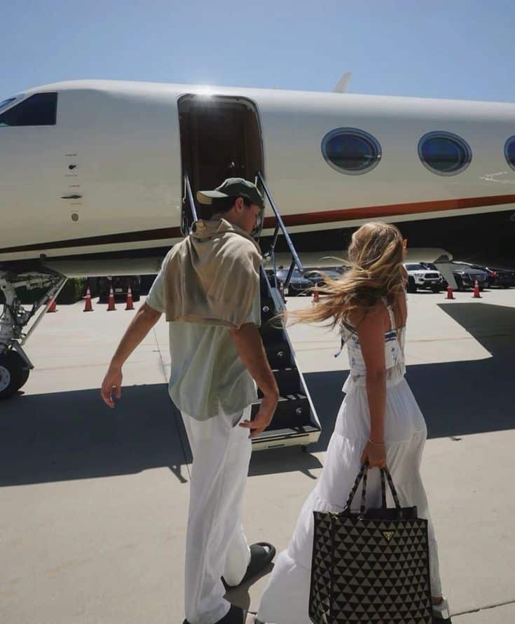 Couple walking towards private jet on sunny day, stylishly dressed, luxury travel concept.