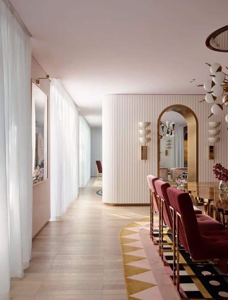 Luxurious dining room with pink chairs, elegant decor, and ambient lighting. Curved walls and large windows create an airy feel.