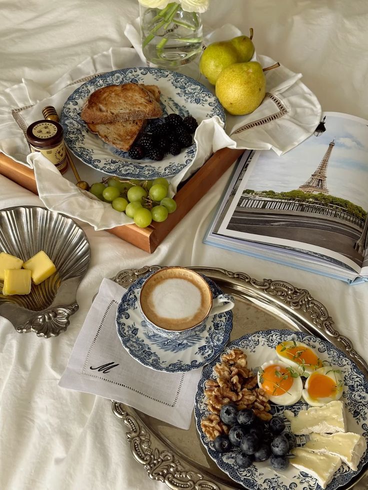 9cc69a98-4eab-445d-aae9-1dac0e706cd8 Elegant breakfast spread with coffee, fruits, eggs, nuts, and cheese on a silver tray next to an open magazine featuring the Eiffel Tower. - Handy Home Elegant breakfast spread with coffee, fruits, eggs, nuts, and cheese on a silver tray next to an open magazine featuring the Eiffel Tower.