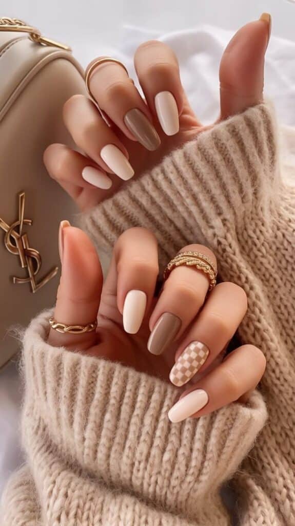 Stylish nude manicure with geometric patterns, gold rings, and neutral sweater for a chic winter look.