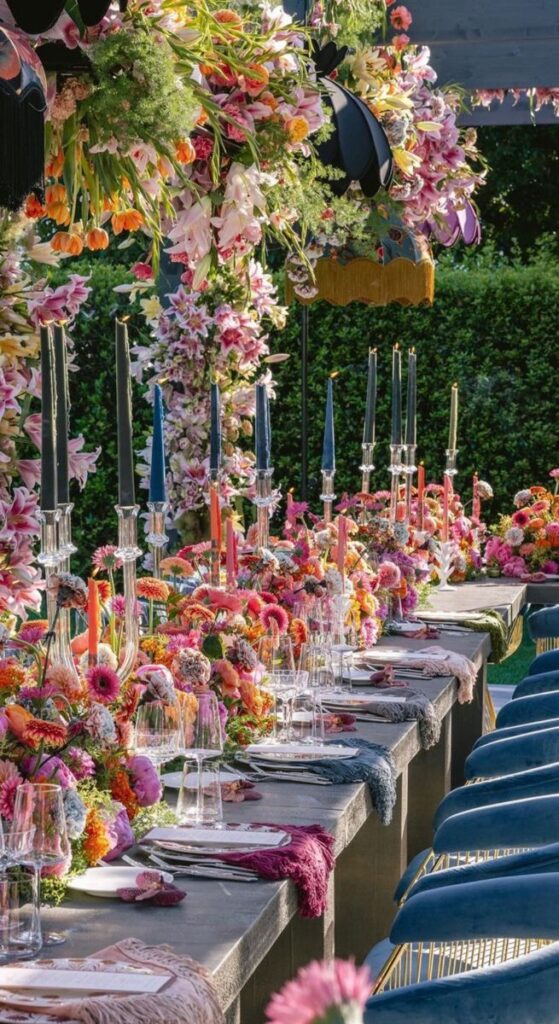 Elegant outdoor dining setup with vibrant floral centerpieces, colorful candles, and lush greenery, perfect for a summer event.
