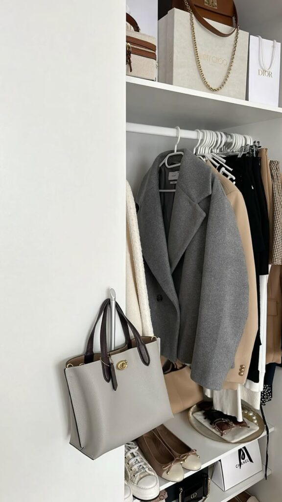 Stylish closet with grey coat, beige handbag, designer boxes, shoes, and accessories neatly organized for a chic wardrobe look.