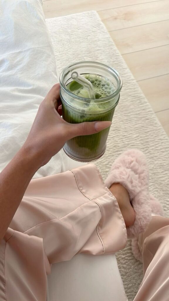 Cozy morning with matcha latte in hand, wearing pink satin pajamas and fluffy slippers on a plush rug. Perfect relaxation moment.