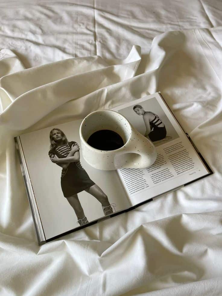 Coffee cup on fashion magazine on a bed, blending style and relaxation on a cozy morning.