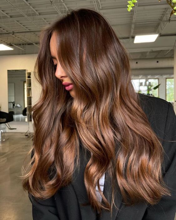 Woman with long, wavy brown hair in a salon, showcasing glossy hair and layered styling.