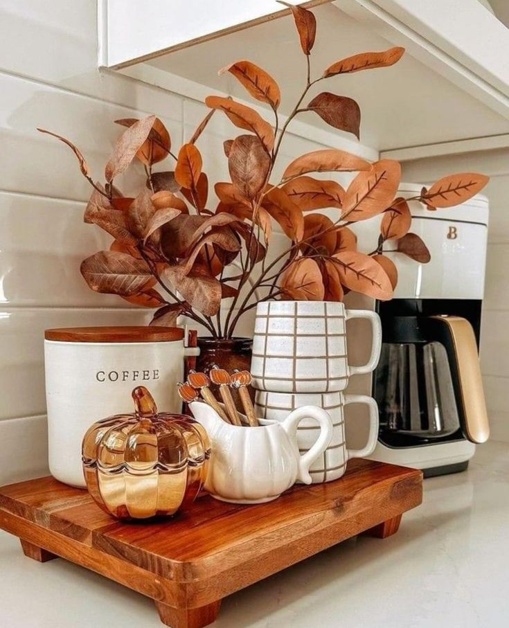 Warm, cozy kitchen corner with coffee canister, mugs, autumn leaves, and decorative pumpkin on a wooden tray. Perfect fall decor.