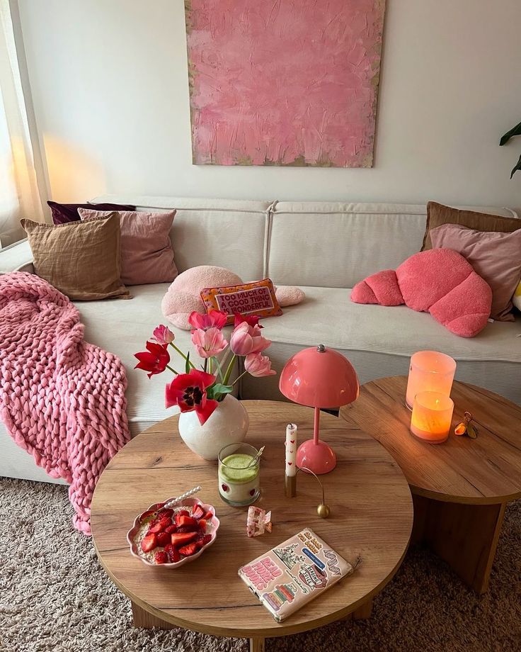 Cozy living room with a pink theme, featuring a sofa, tulips, candles, and a stylish coffee table setup with snacks and a lamp.