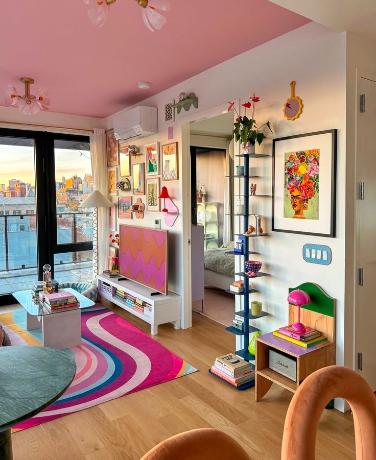 Colorful living room with pink ceiling, vibrant decor, wall art, patterned rug, and city view. Cozy, eclectic interior design.