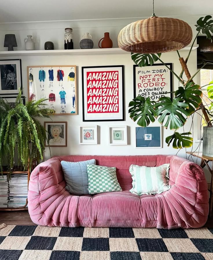 Cozy living room with pink sofa, patterned cushions, art-filled gallery wall, wicker pendant, and lush plants for a stylish vibe.